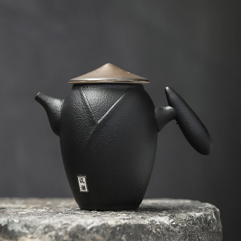 Black teapot with round lid, isolated on gray stone background.