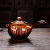A side view of a patterned brown teapot with a shiny surface on a wooden table.