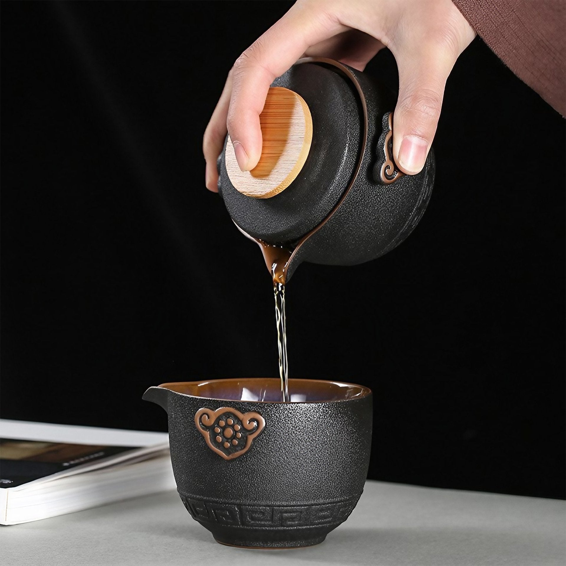 Pouring tea into ornate black cup from teapot, dark background.