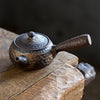 Rustic ceramic teapot on a wooden log, side view.