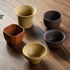 Assorted tea cups in different shapes and earthy tones displayed on a wooden surface.