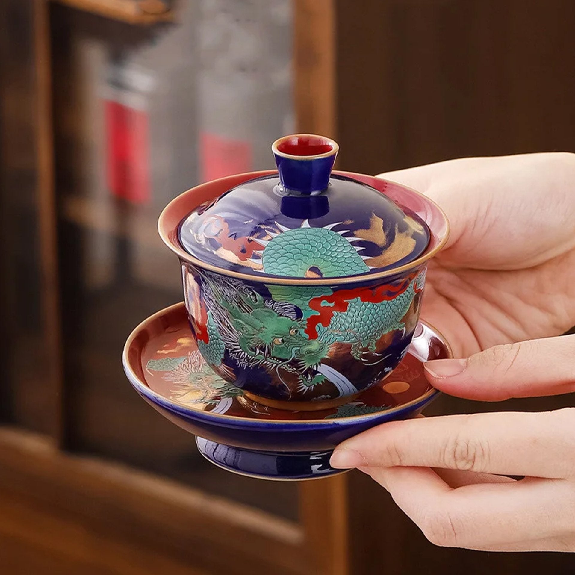 Holding a dragon-patterned gaiwan over a matching saucer.