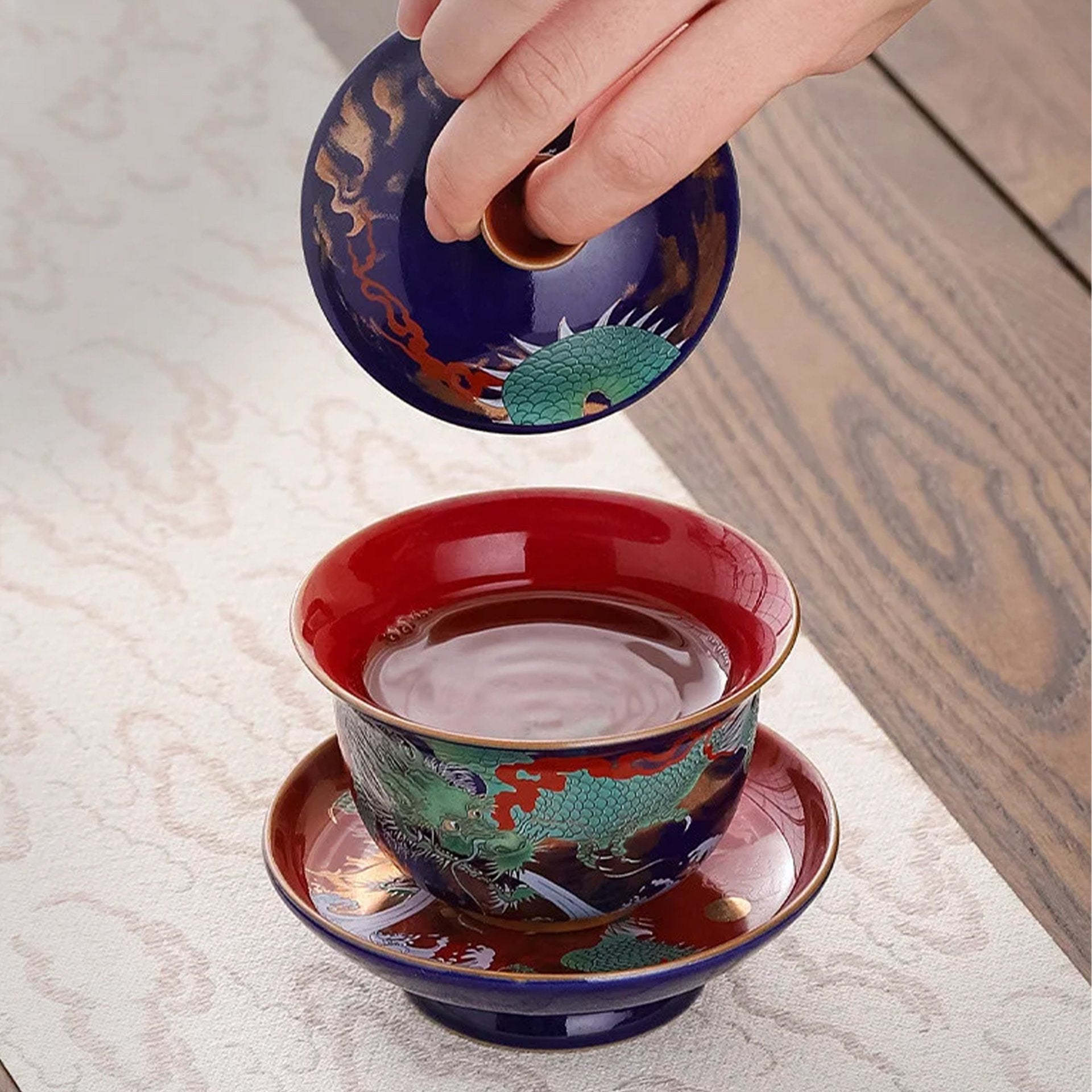 Dragon motif gaiwan held in hand over a red saucer.