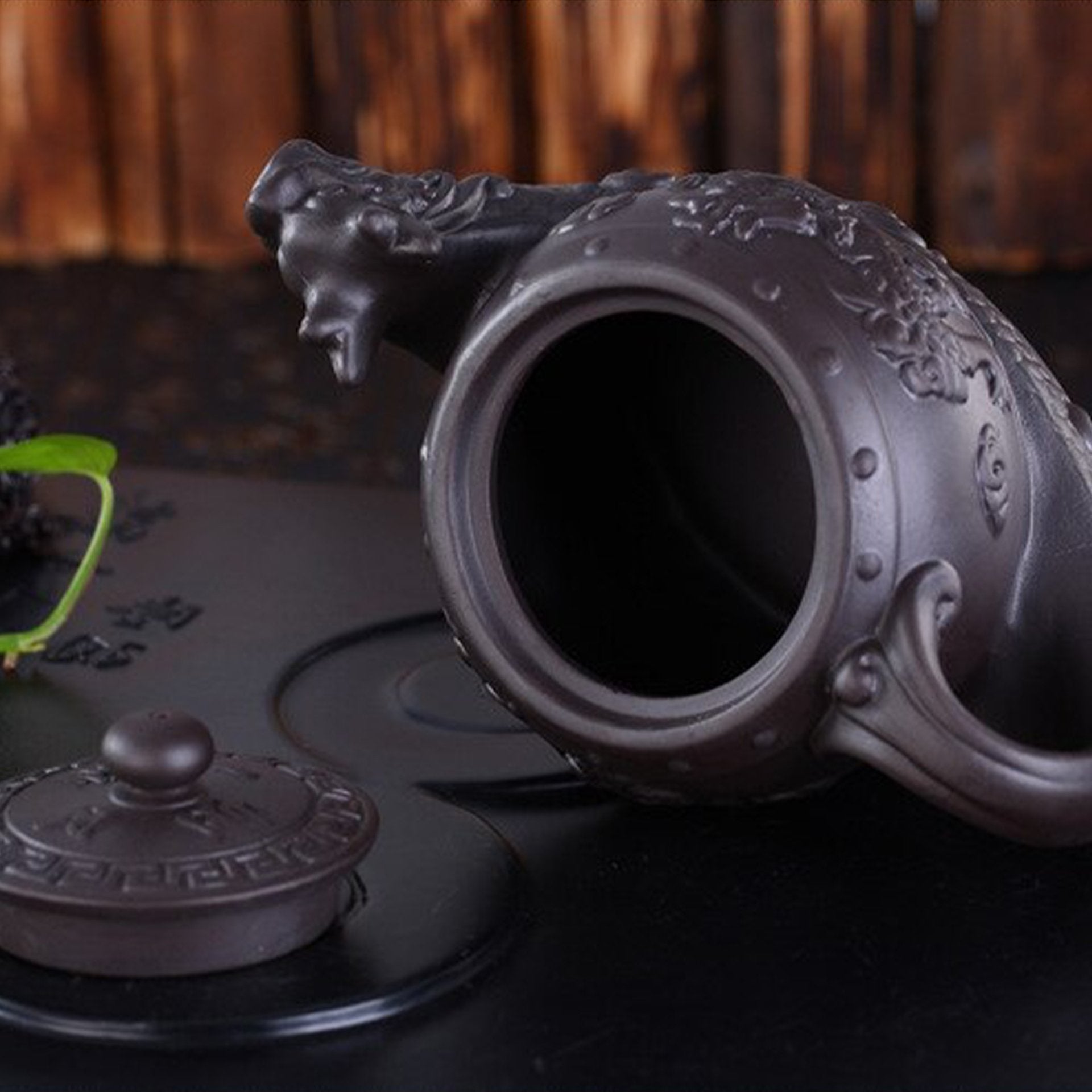 Open dark clay teapot with dragon design and lid off, showing the interior.