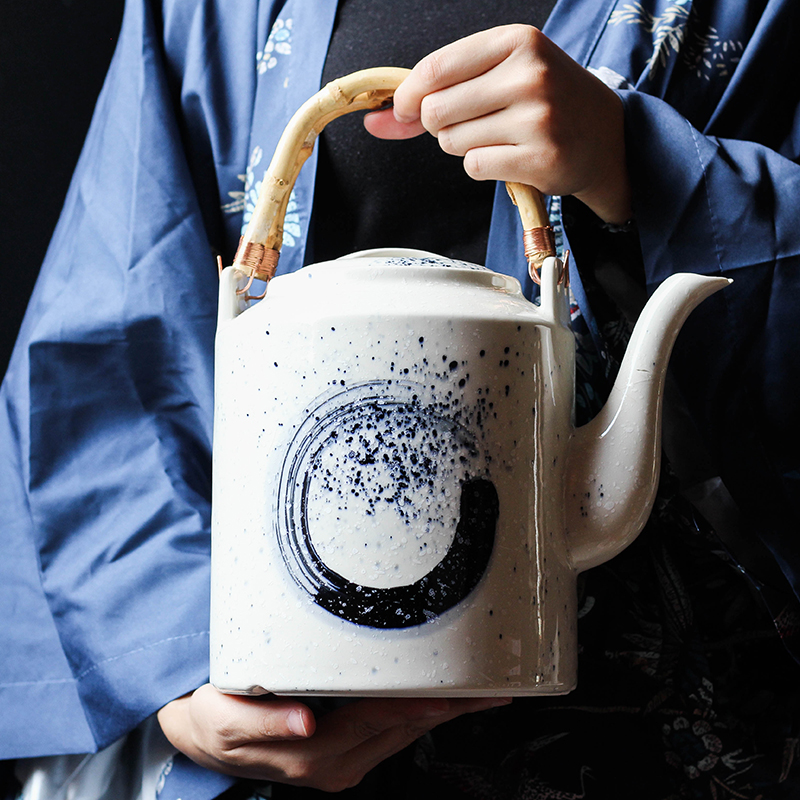 Person in blue kimono pouring tea from a white teapot with black circle design.