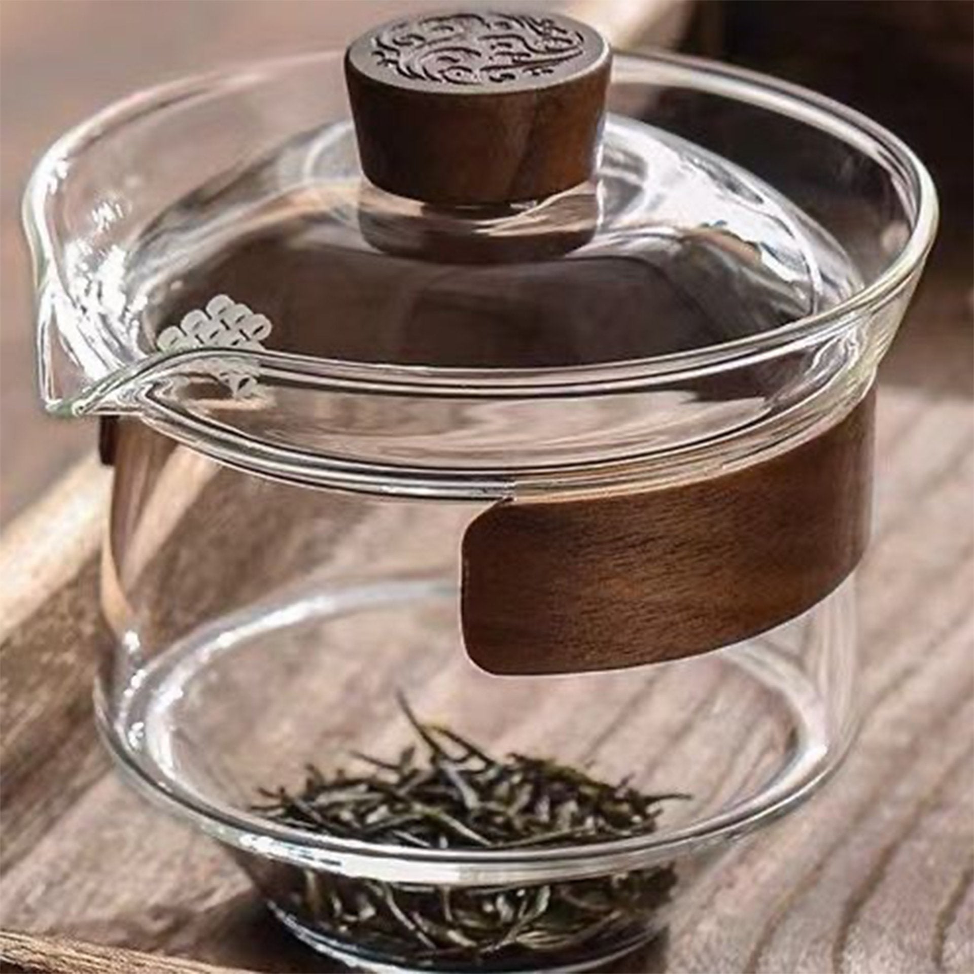 Transparent glass teapot with wooden handle and loose green tea leaves