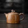 Brown glazed teapot with lion detail on lid, set on a dark wooden table