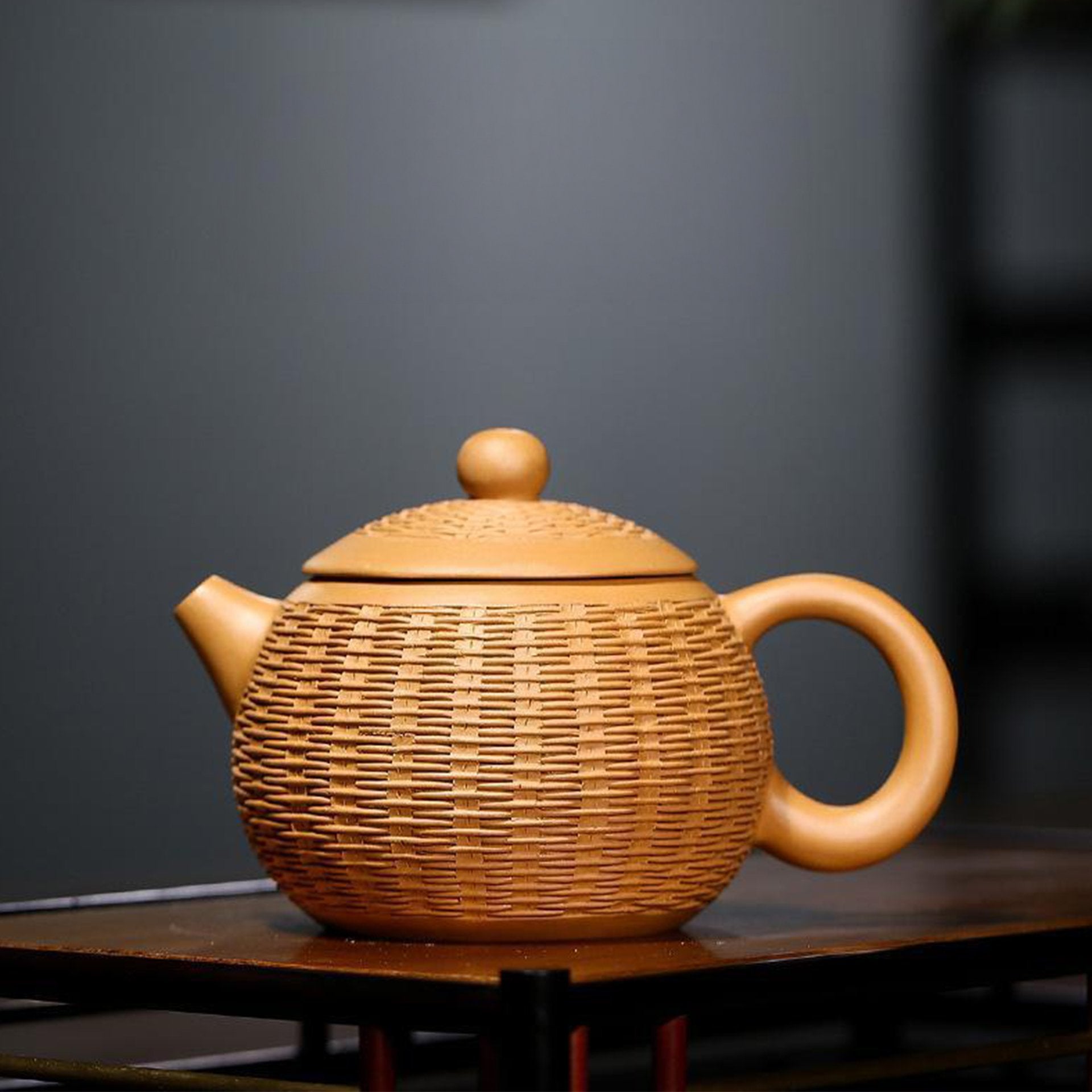 Golden textured teapot on a shelf in a dark room.