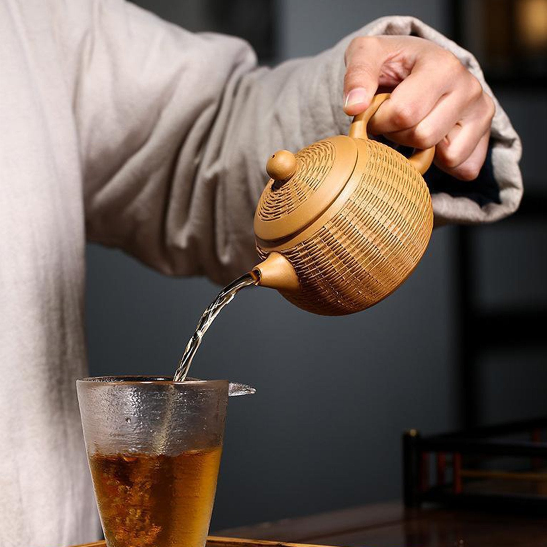 Hand pouring tea from a golden textured teapot into a glass.