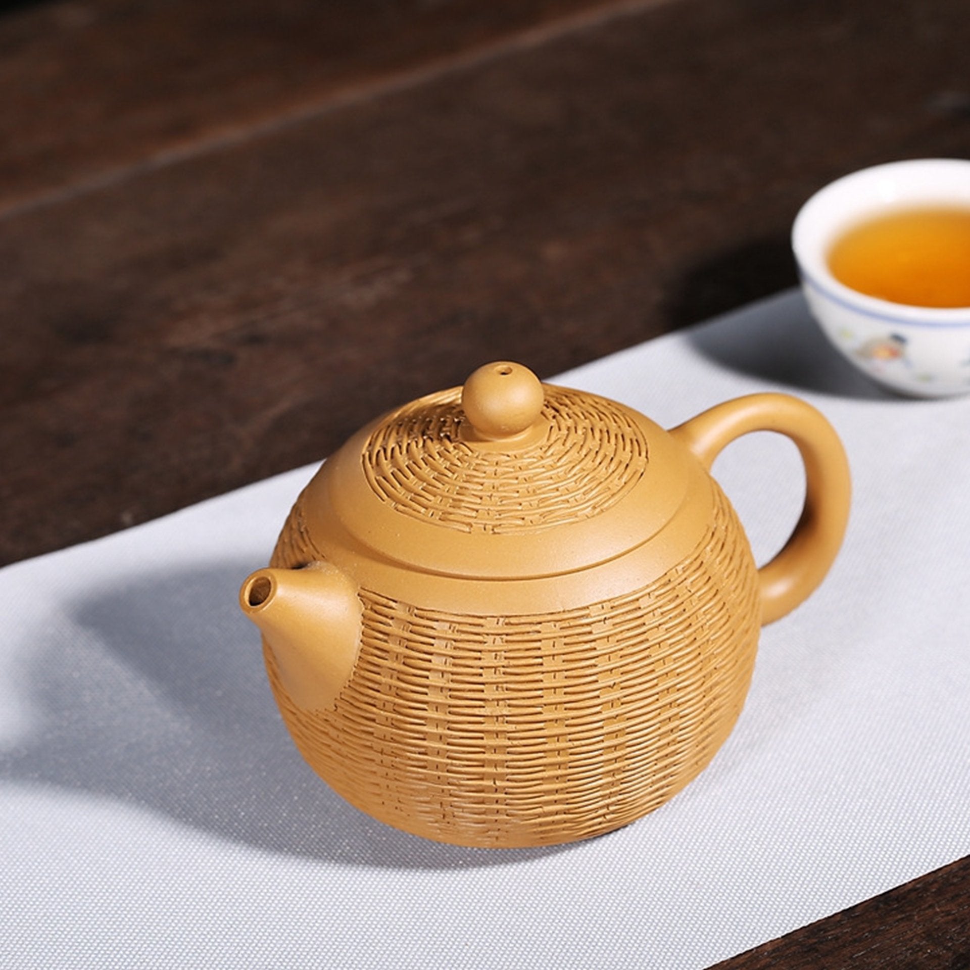 Golden textured teapot on a white surface beside a tea cup.