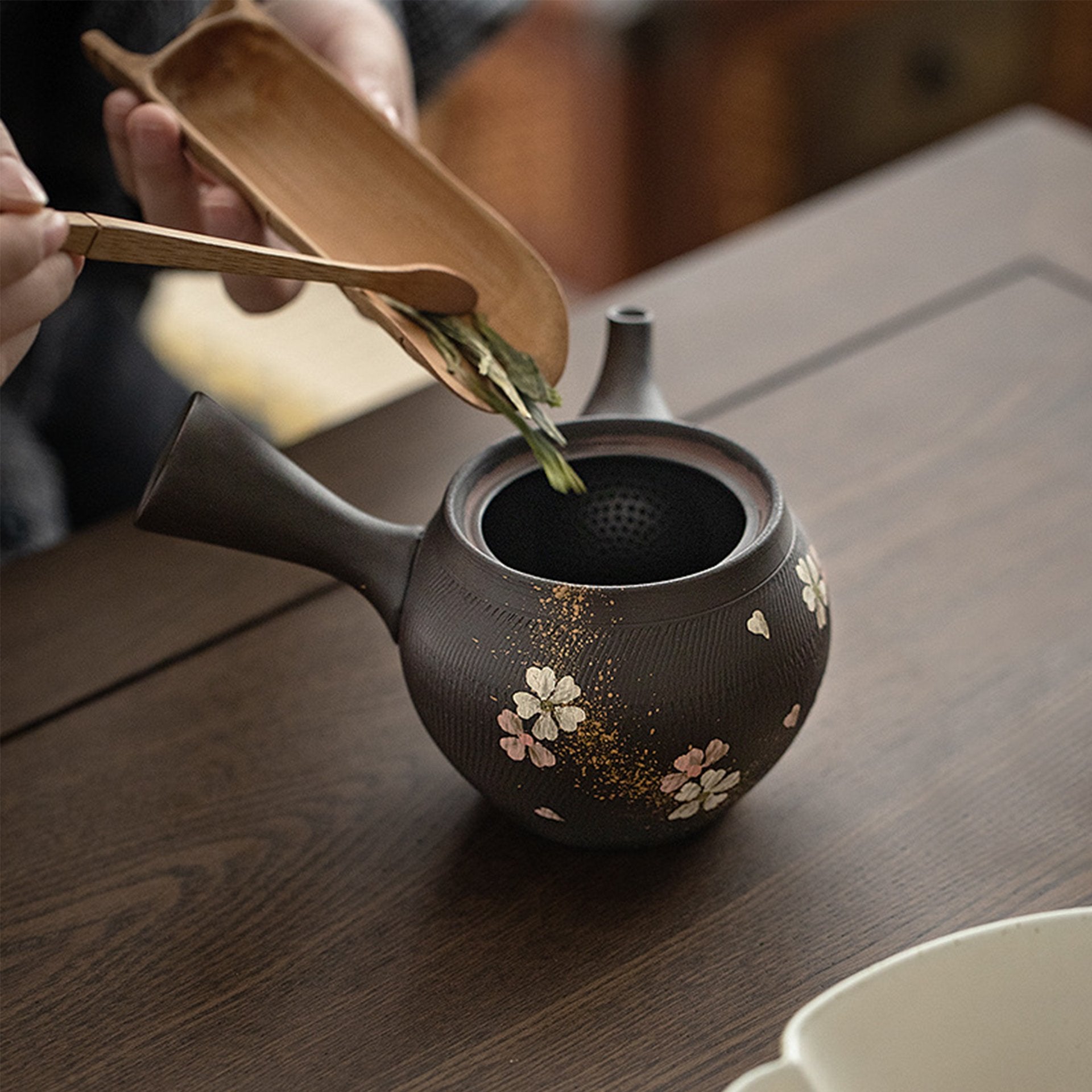 Person pouring tea from a dark teapot adorned with gold and floral motifs.