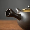 Close-up of a dark teapot spout on a wooden table.
