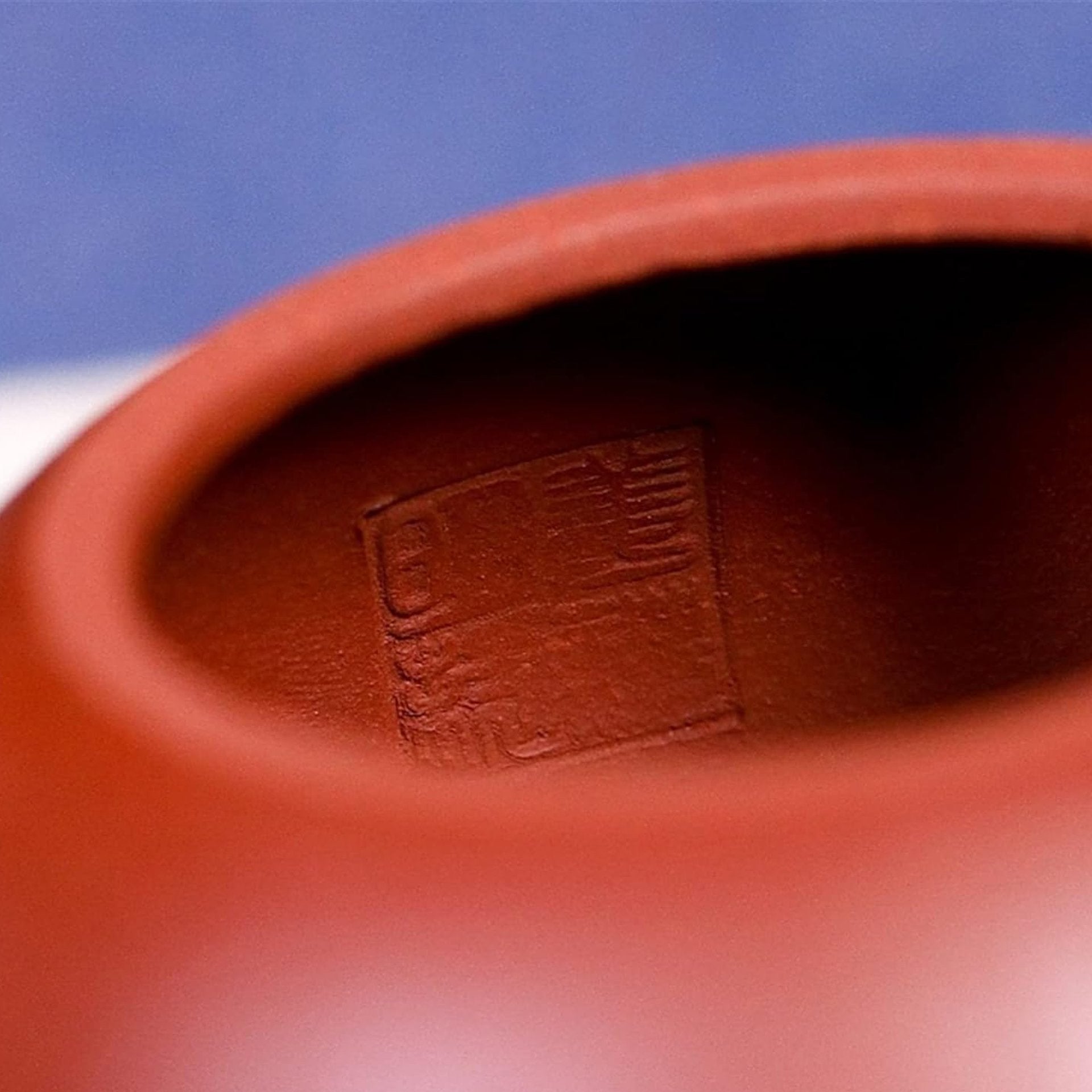Close-up of red teapot held in hand, showing the delicate engravings and design.