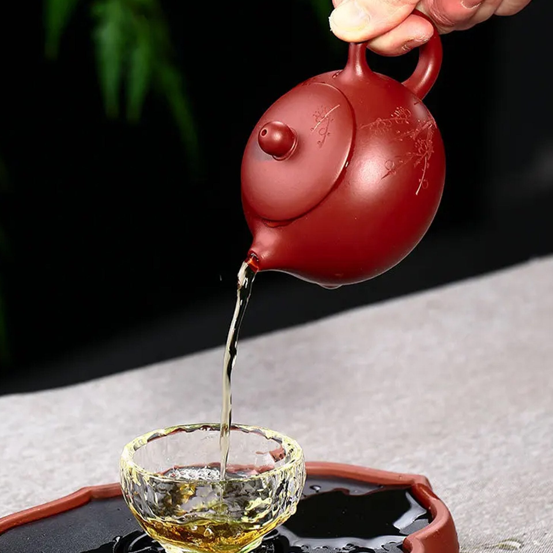 Red teapot pouring tea into a glass cup, demonstrating elegant flow and precision.