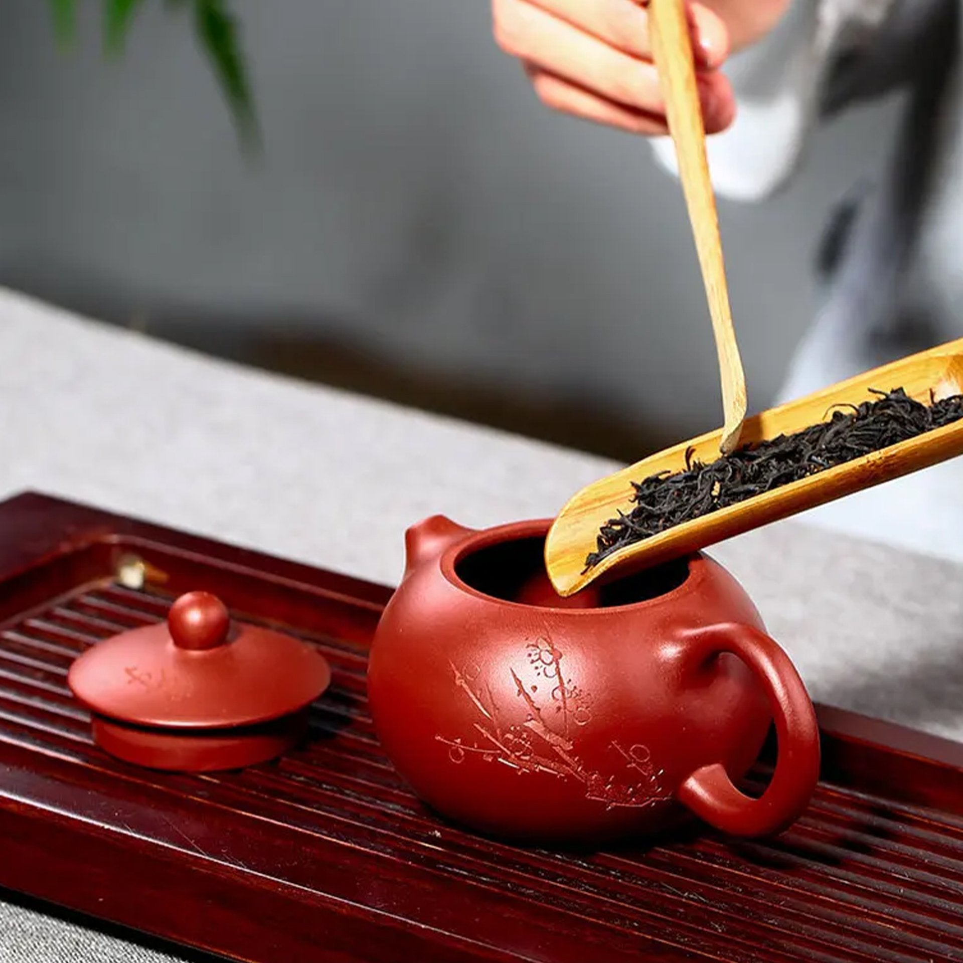 Hand filling a red clay teapot with loose black tea, showcasing traditional tea preparation.