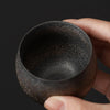 Hand holding a black ceramic tea bowl with shiny interior