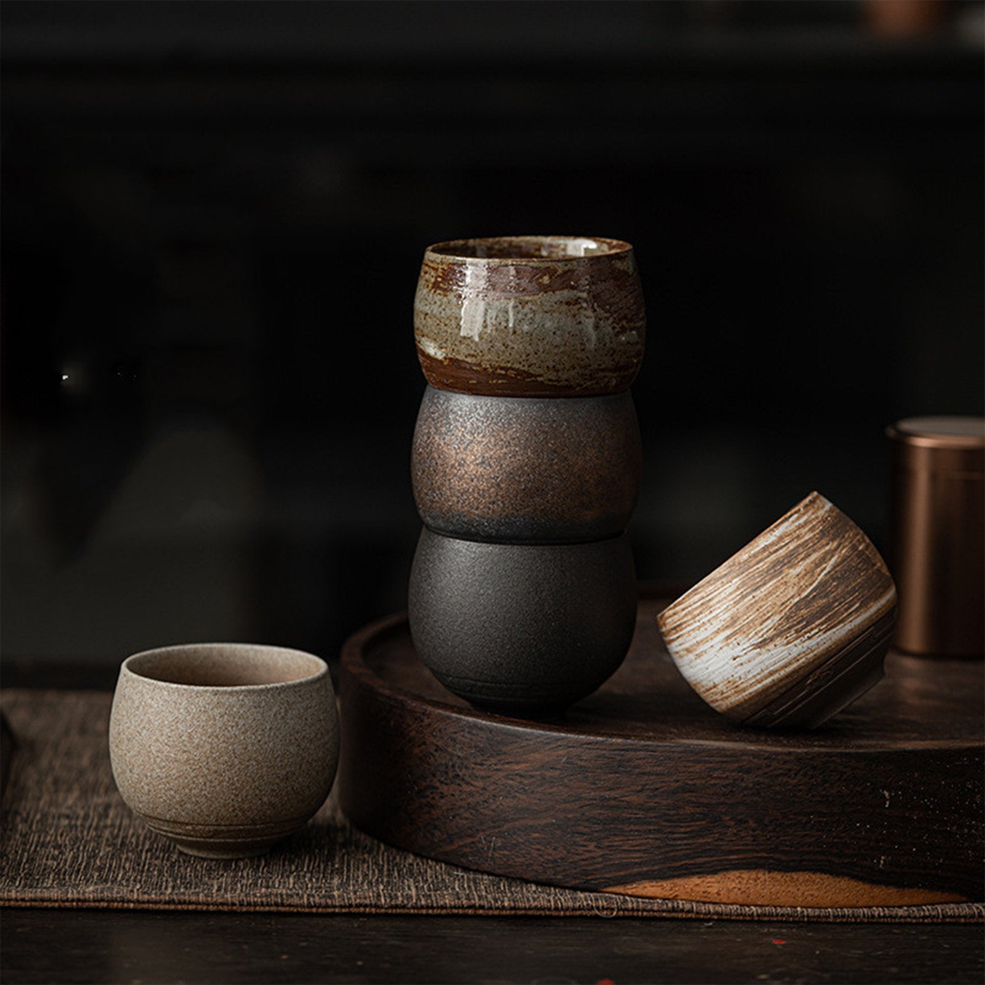 Stacked ceramic tea bowls in brown, black, and beige on wooden tray