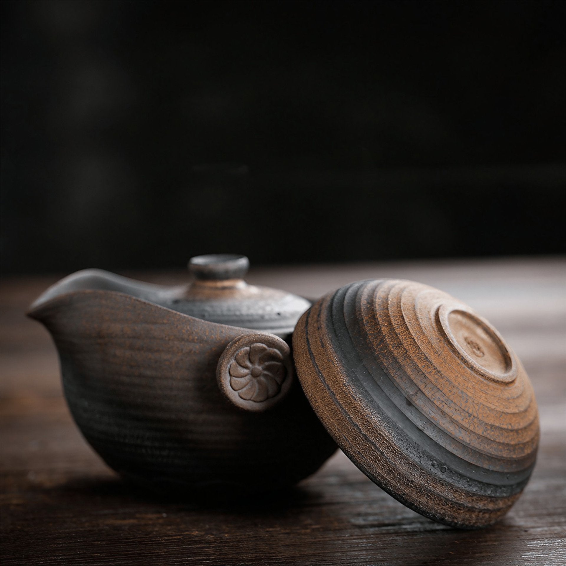 Open textured ceramic teapot with lid off to the side, showcasing a floral motif on the body, on a wooden surface.