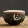 A Japanese tea cup with a textured brown and green glaze, featuring a painted white crane
