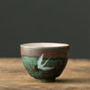 A Japanese tea cup with a textured brown and green glaze, featuring a painted white crane.