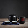 A Japanese travel tea set with two cups, a black teapot with a red detail, and a carry case.