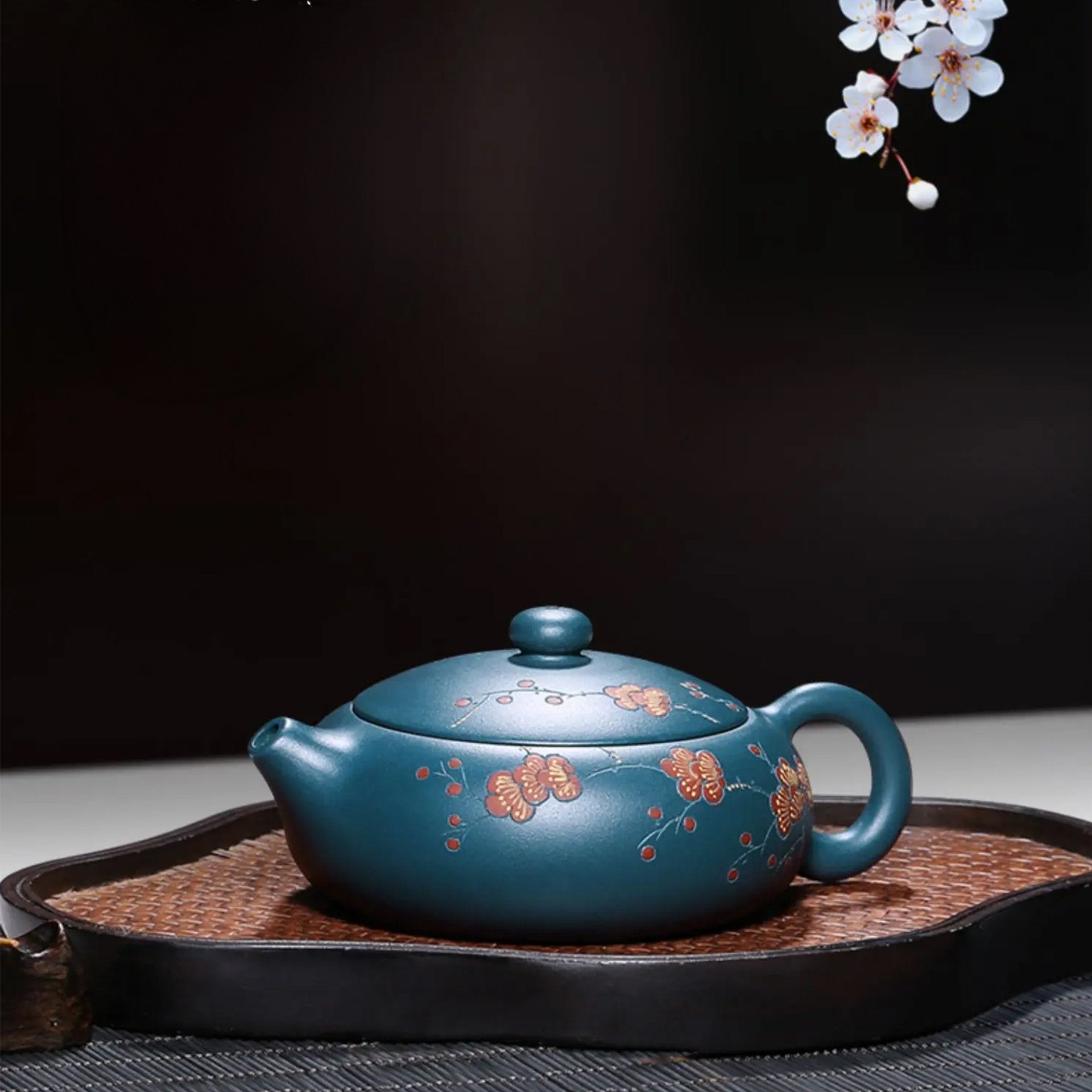 Floral-patterned blue teapot on a tray with a cherry blossom background.