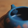 Close-up of a blue teapot's spout featuring a filter inside.