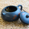 Open blue teapot with dried tea leaves inside beside its lid.