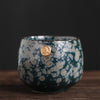 Textured blue Japanese teacup with a gold seal on a wooden table.