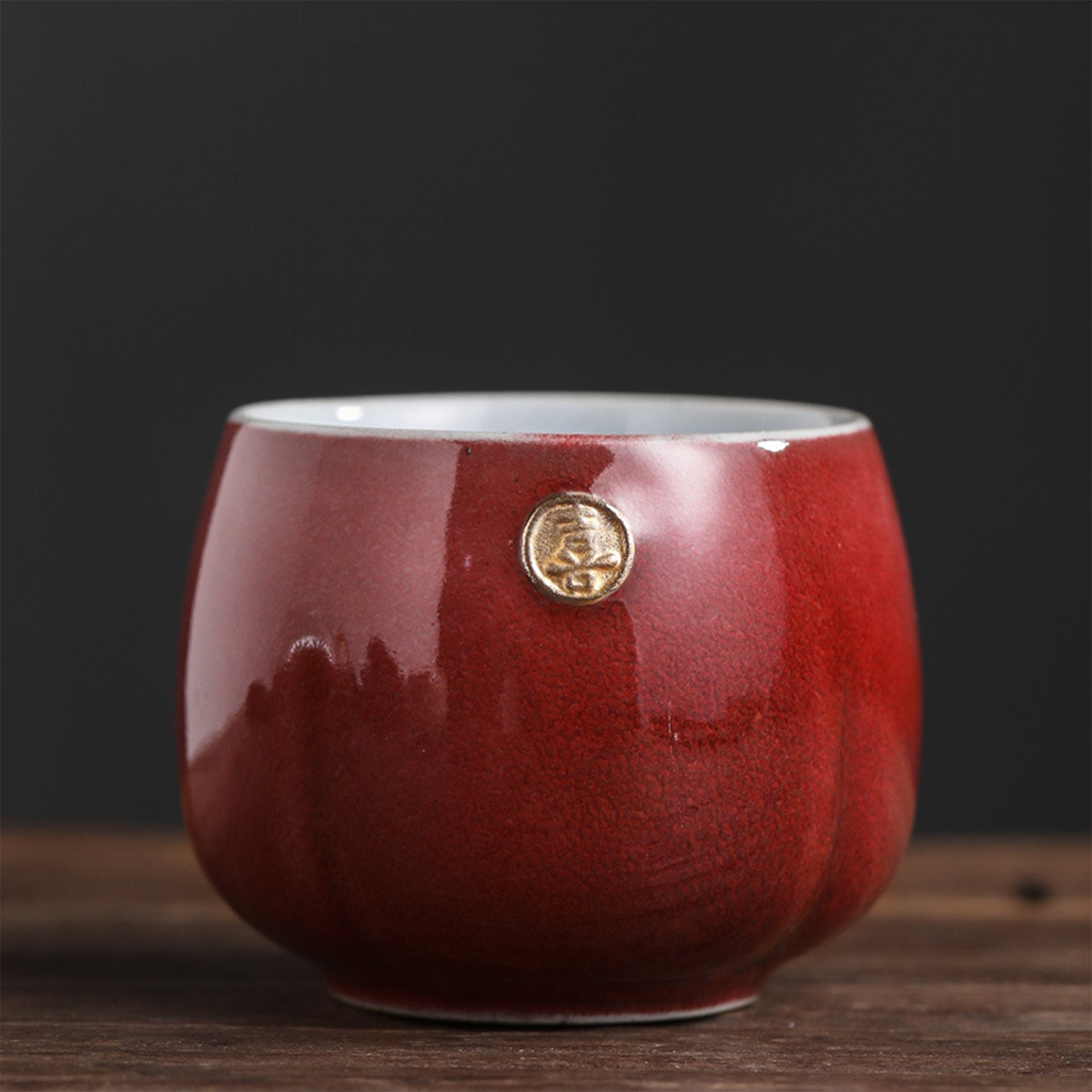 Glossy red Japanese teacup with a gold seal against a dark background.
