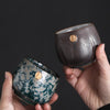 Two hands holding a pair of Japanese teacups, one blue and one brown.