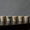 Five small porcelain tea cups with traditional Japanese designs, displayed in a row against a muted backdrop.