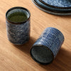 Two patterned blue ceramic cups, one with tea, on a wooden surface.