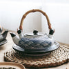 A teapot with a blue wave pattern and a bamboo handle on a woven mat.