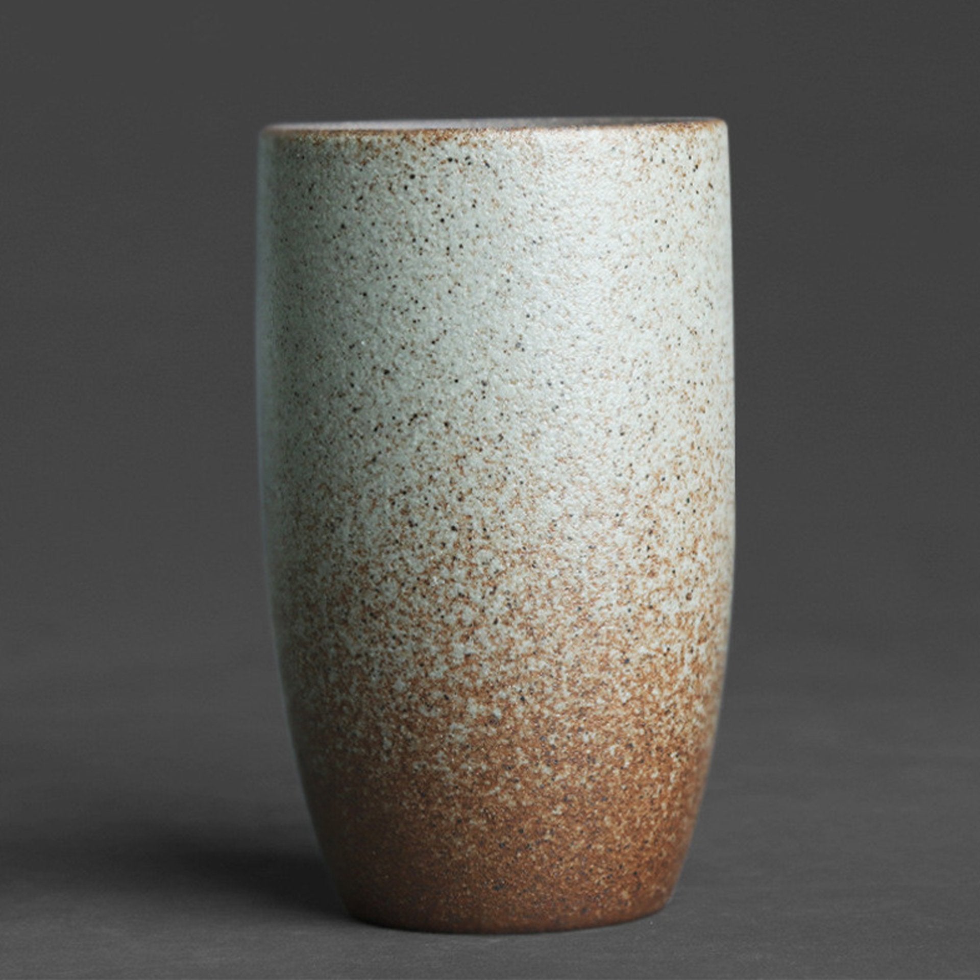 Tall beige ceramic cup on a gray background, featuring a speckled design.