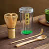 Matcha tea set with bamboo whisk, scoop, and spoon on a wooden surface.