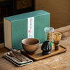 Matcha tea set with bowl, whisk, holder, spoon, scoop,tea towel on a tray, with a packaged box in the background.