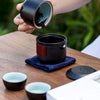 Hand holding black ceramic tea cup over a pot on a napkin.