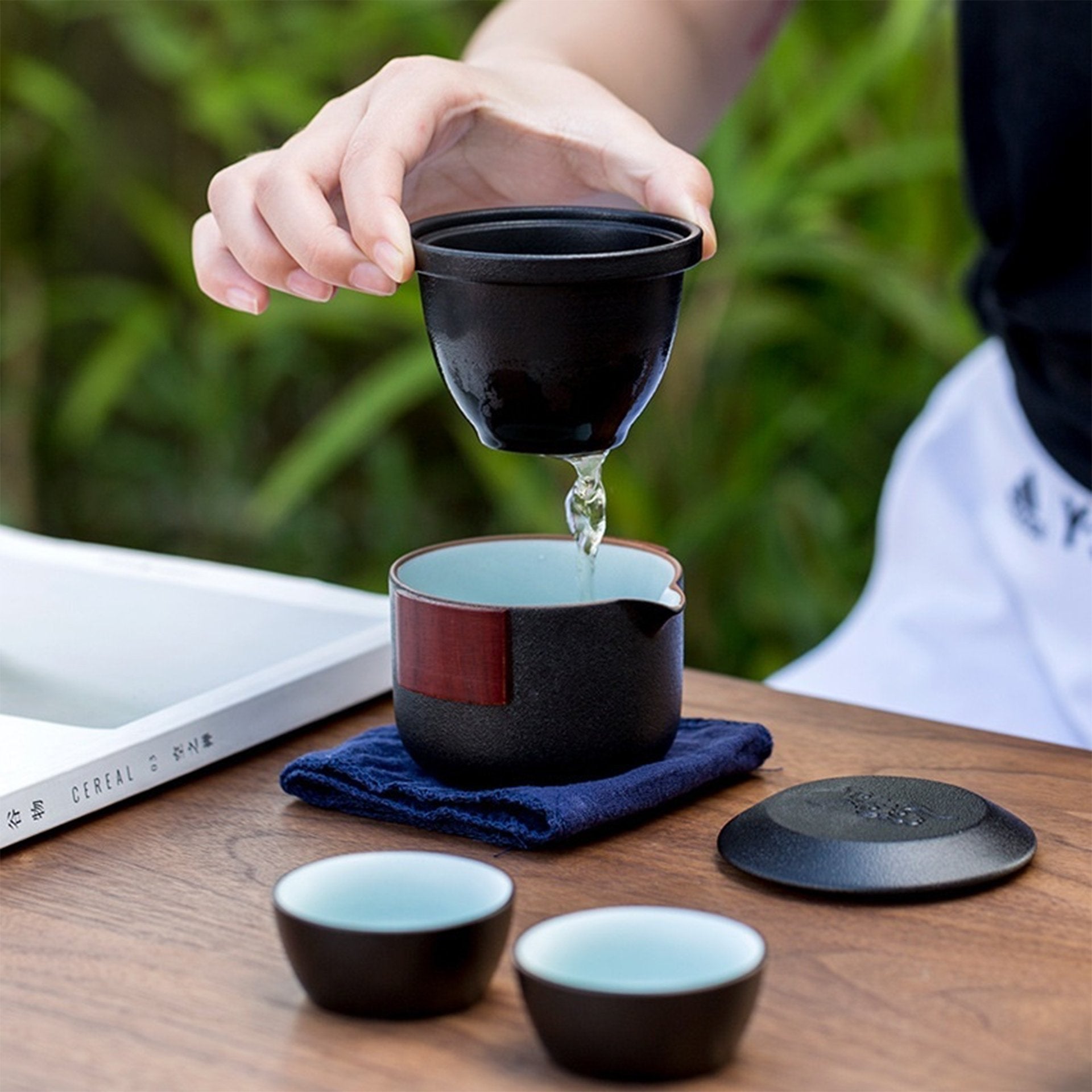 Pouring tea from black ceramic pot to cups on a table.
