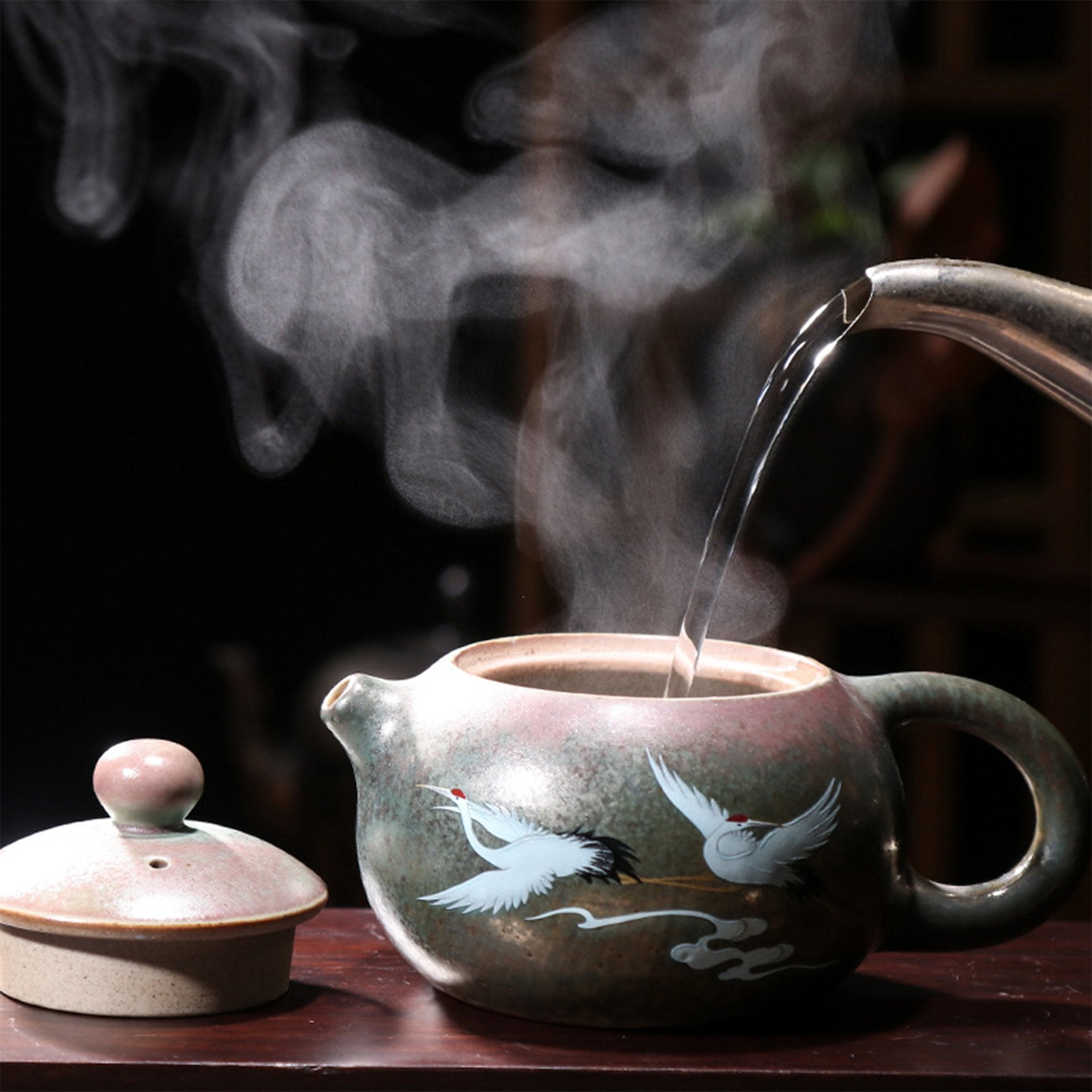 Steaming painted teapot with crane designs being filled with water