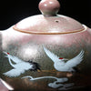 Painted teapot with white cranes and golden accents on dark background