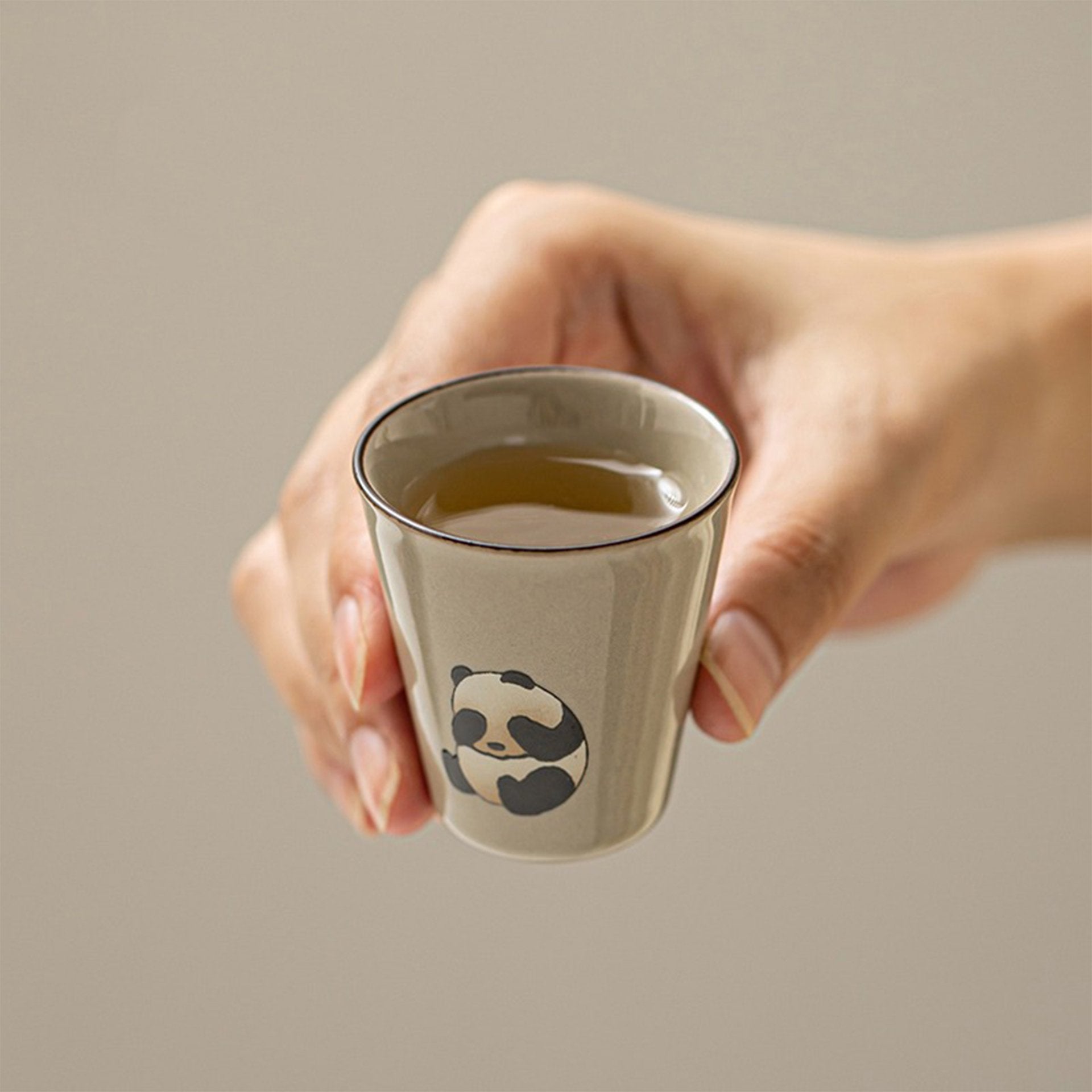 Hand holding a teacup with tea, panda design visible from the front.