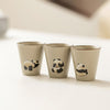 Set of three beige teacups with different panda designs, aligned on white.