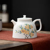 Elegant white floral teapot on a red mat, close-up view.