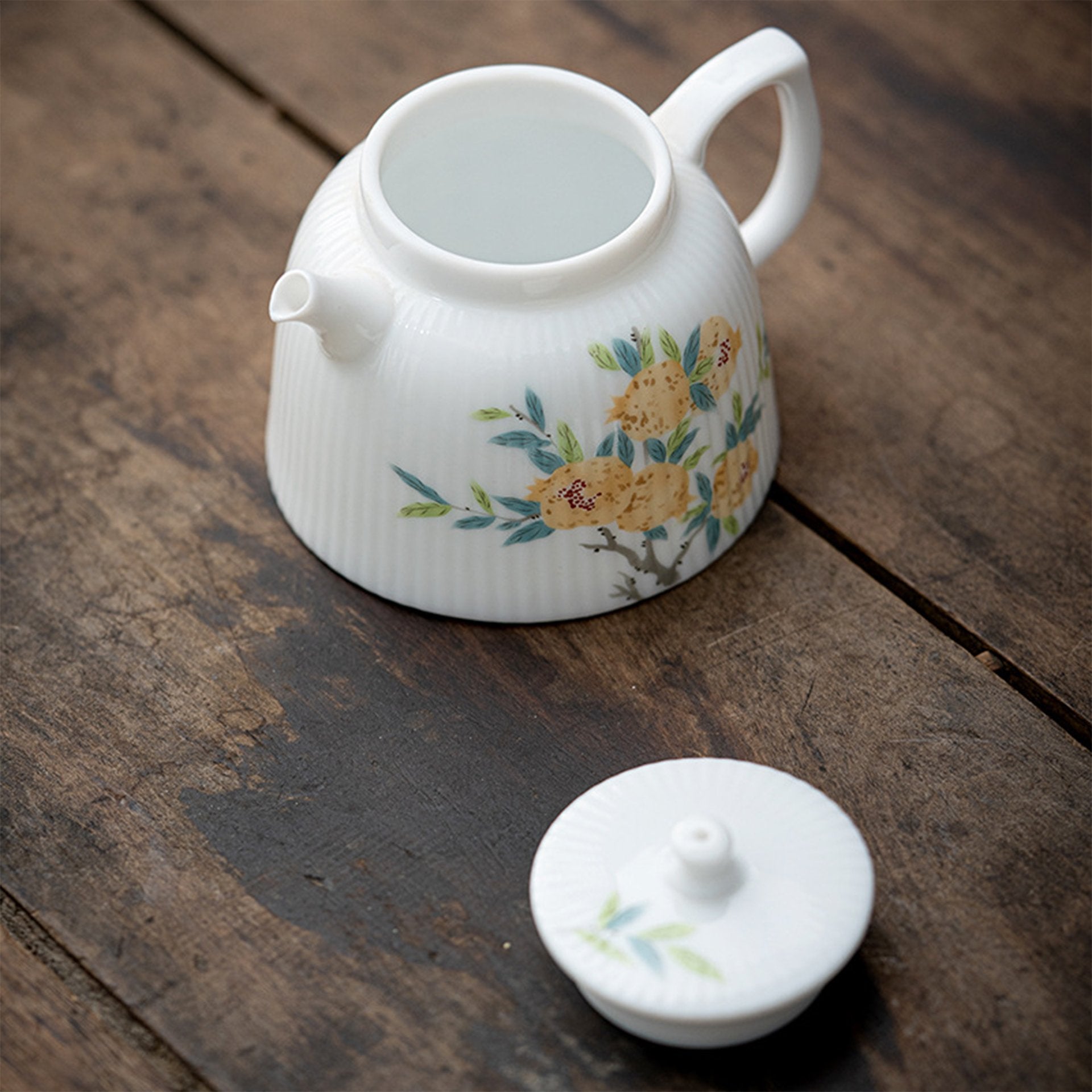 Teapot with lid off on rustic wooden surface, white with floral pattern.