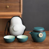 Teal teapot and two cups with white carrying case on wooden table.