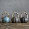 Three rustic teapots with fiber handles on a wooden surface.