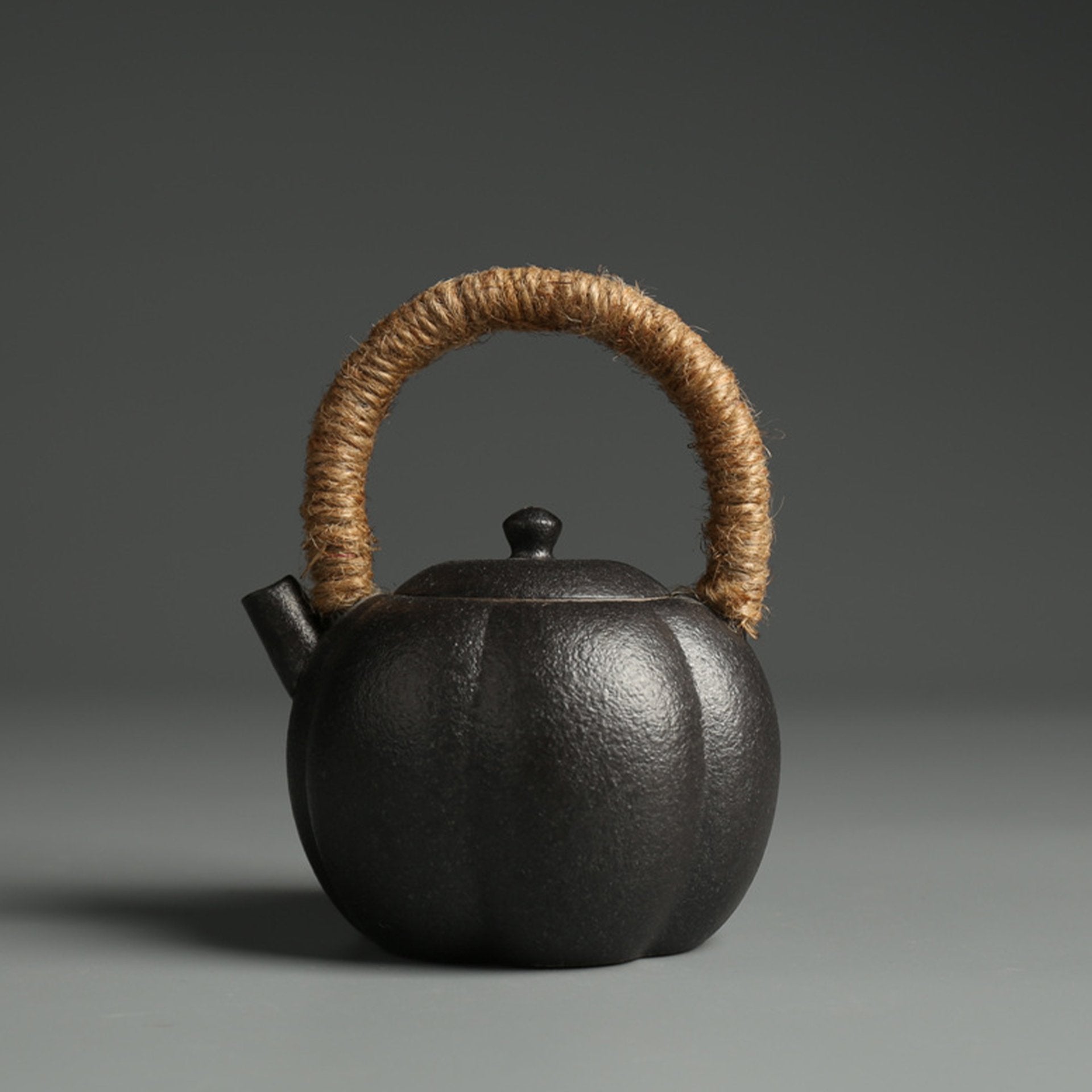 Black rounded teapot with a natural fiber handle against a dark background.