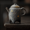 Dark textured teapot with gold koi patterns on a wooden surface.