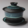 Blue and black textured ceramic tea bowl with lid on plate.